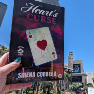 A copy of Heart's Curse is held up, traveling over the Vegas Strip